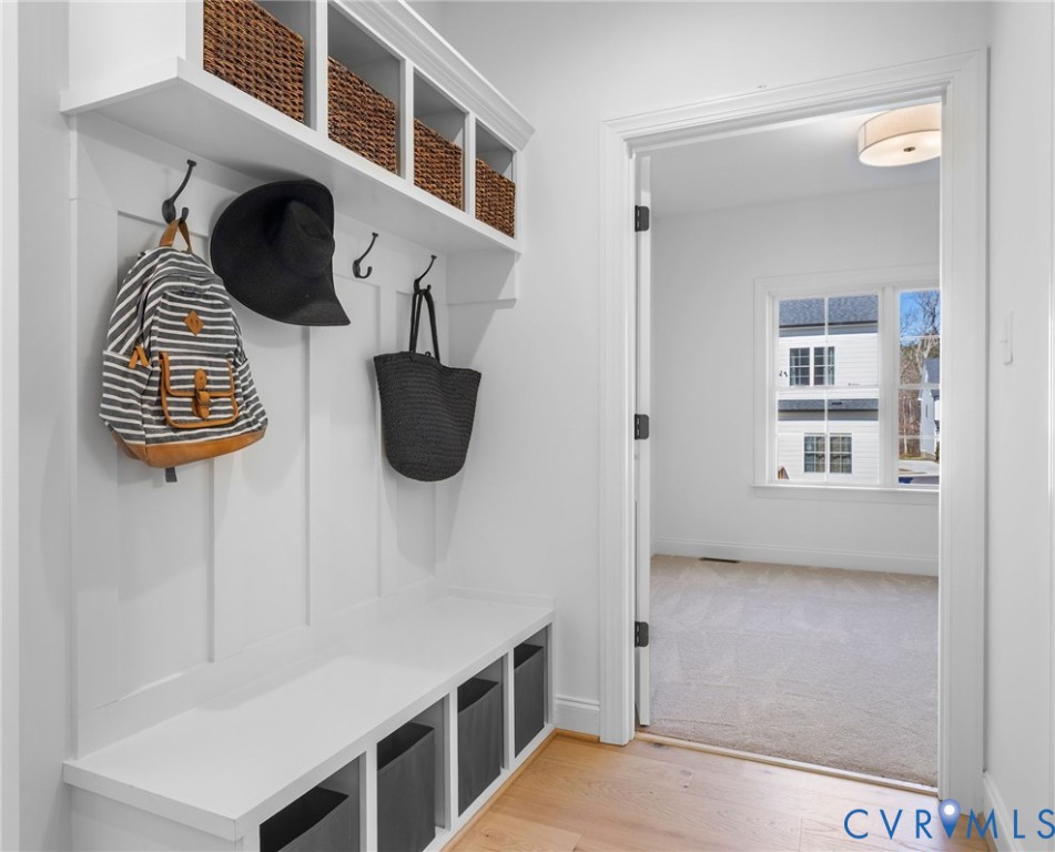 Built-in white mudroom bench featuring board and batten paneling, upper storage cubbies, matte black hooks, and wood-finish flooring