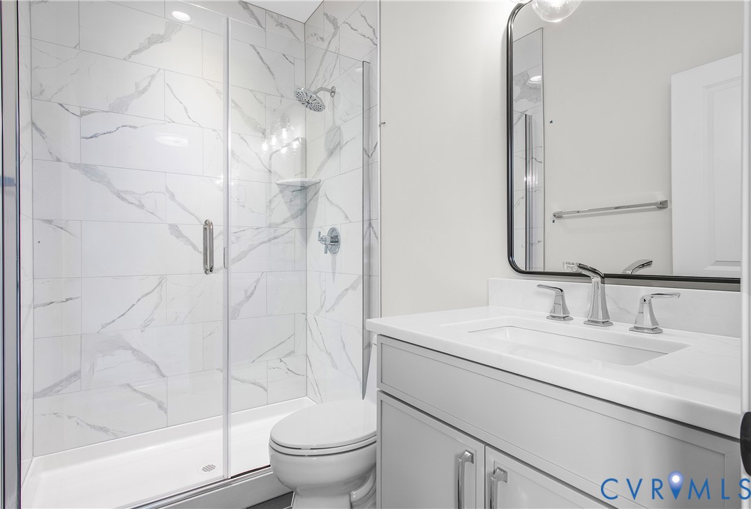 Bathroom featuring a walk-in shower with floor-to-ceiling veined tile surrounds, a glass enclosure, a white vanity with a composite countertop, and a framed mirror
