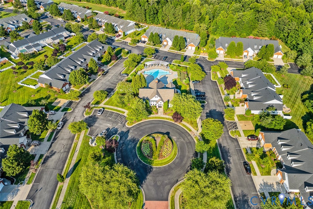 Aerial perspective of a multi-unit residential community featuring a central circular garden, swimming pool, structured parking areas, and mature tree-lined landscaping