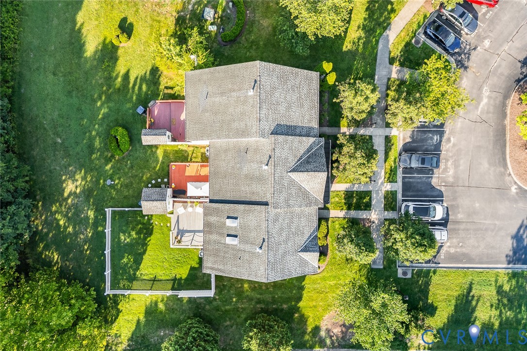 Aerial perspective of property featuring shingled roofing, multiple skylights, and tiered outdoor decks within a fenced-in grassy lawn