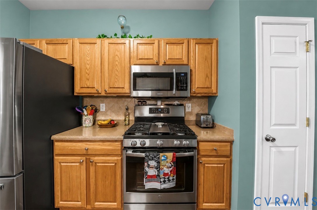 Kitchen featuring wood cabinetry, stainless steel gas range, over-the-range microwave, solid-surface countertops, and tiled backsplash