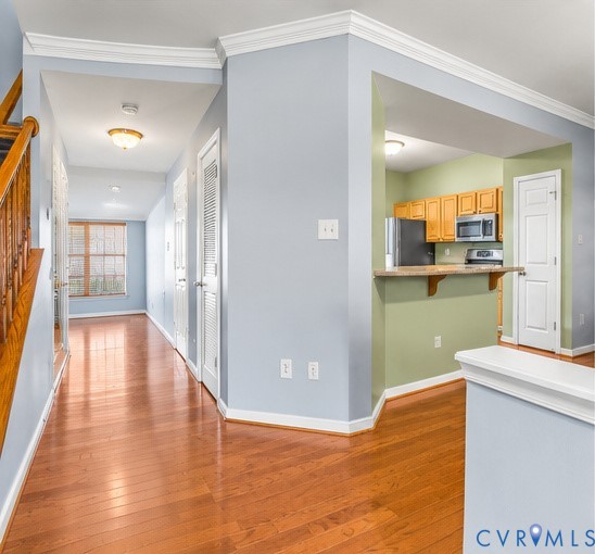 Wood-finish flooring, crown molding, kitchen with a peninsula counter, wood cabinetry, and recessed lighting