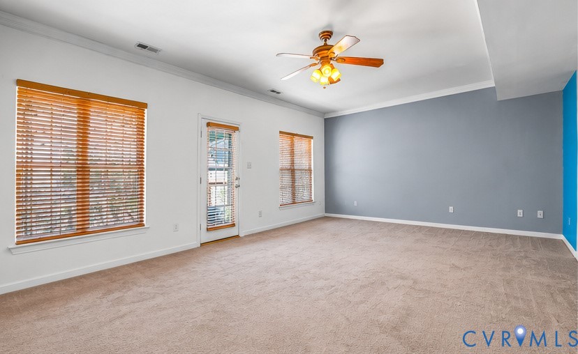 Spacious room featuring carpeting, crown molding, a ceiling fan with integrated lighting, wood-slat window blinds, and a glass-paneled exterior door