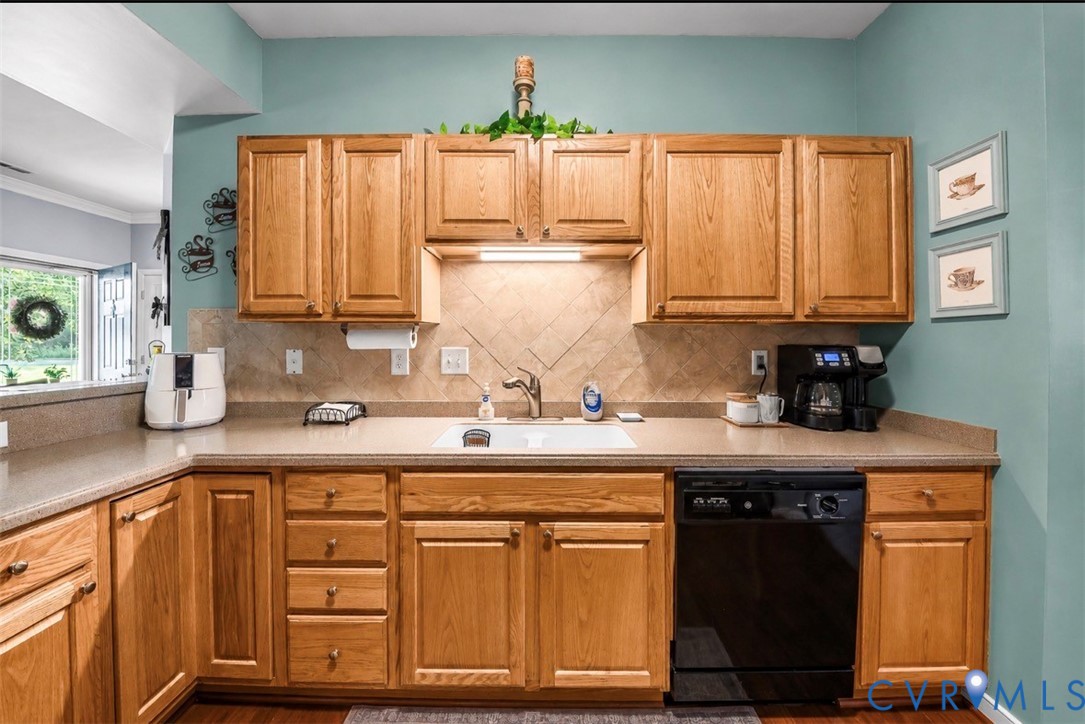 Kitchen featuring natural wood cabinetry, solid surface countertops, a white undermount sink, a diagonal-patterned tile backsplash, and a black dishwasher