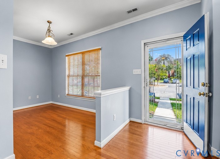 Entryway featuring wood-finish flooring, a six-panel door, decorative metal-frame screen door, crown molding, and a pendant light fixture