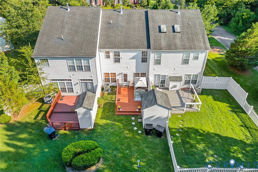 Multi-level exterior featuring light-toned horizontal siding, multi-sectional wood-tone decking, two detached storage structures, and a fenced yard Multi-level exterior featuring light-toned horizontal siding, multi-sectional wood-tone decking, two detached storage structures, and a fenced yard