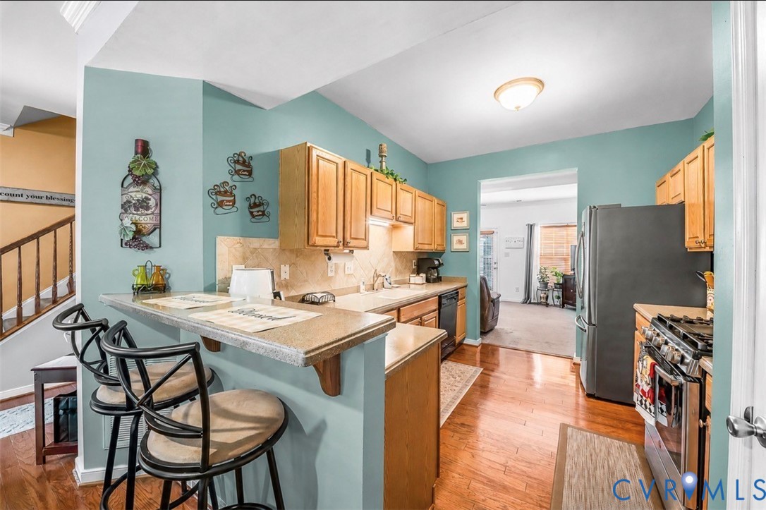 Kitchen featuring wood-finish cabinetry, a breakfast bar with solid-surface countertop, stone-tile backsplash, and wood-finish flooring