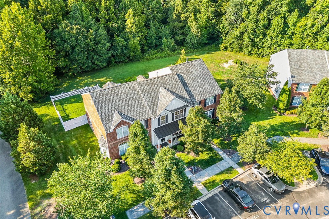 Multi-story brick and siding exterior featuring an asphalt shingle roof, white vinyl fencing, concrete walkways, and mature landscaping
