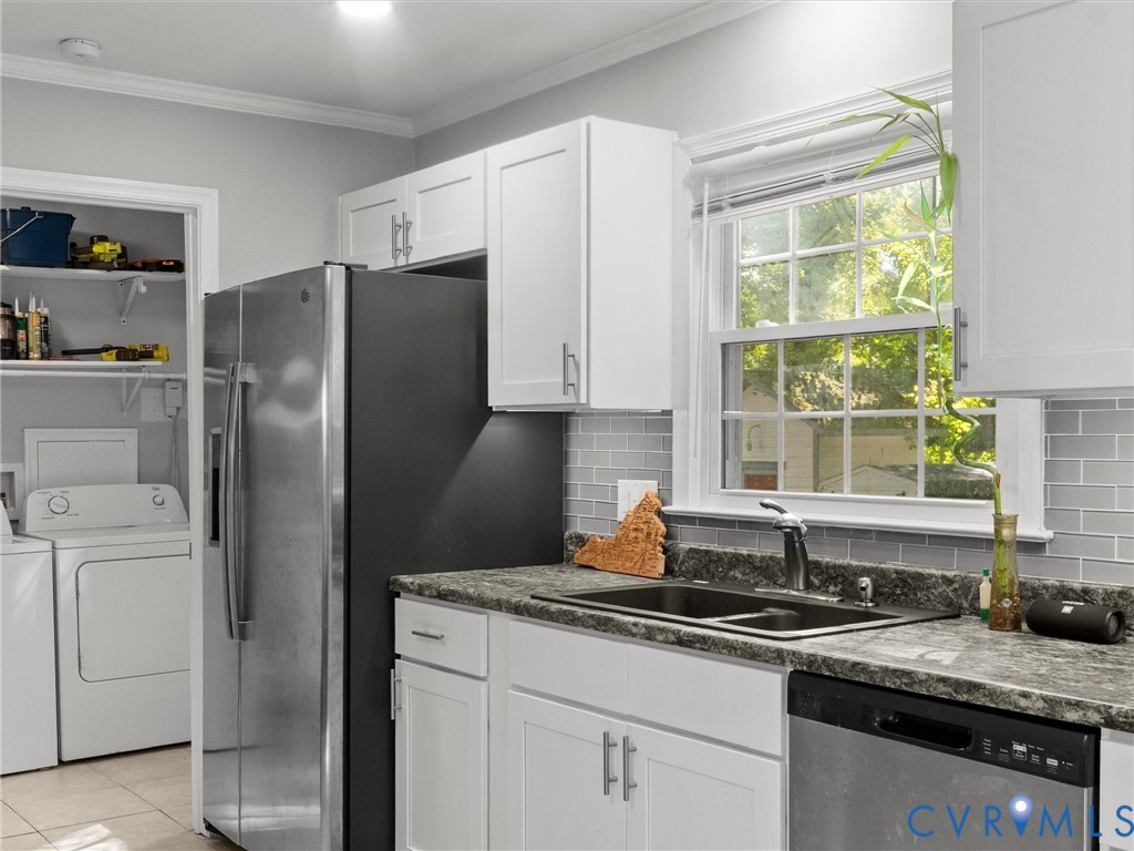 Kitchen featuring white shaker-style cabinetry, dark stone-patterned countertops, gray subway tile backsplash, stainless steel appliances, and a double-basin sink