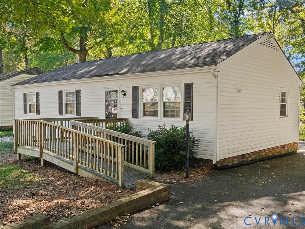 White vinyl siding exterior featuring a gable roof, wood-finish ramp, asphalt driveway, and brick garden edging