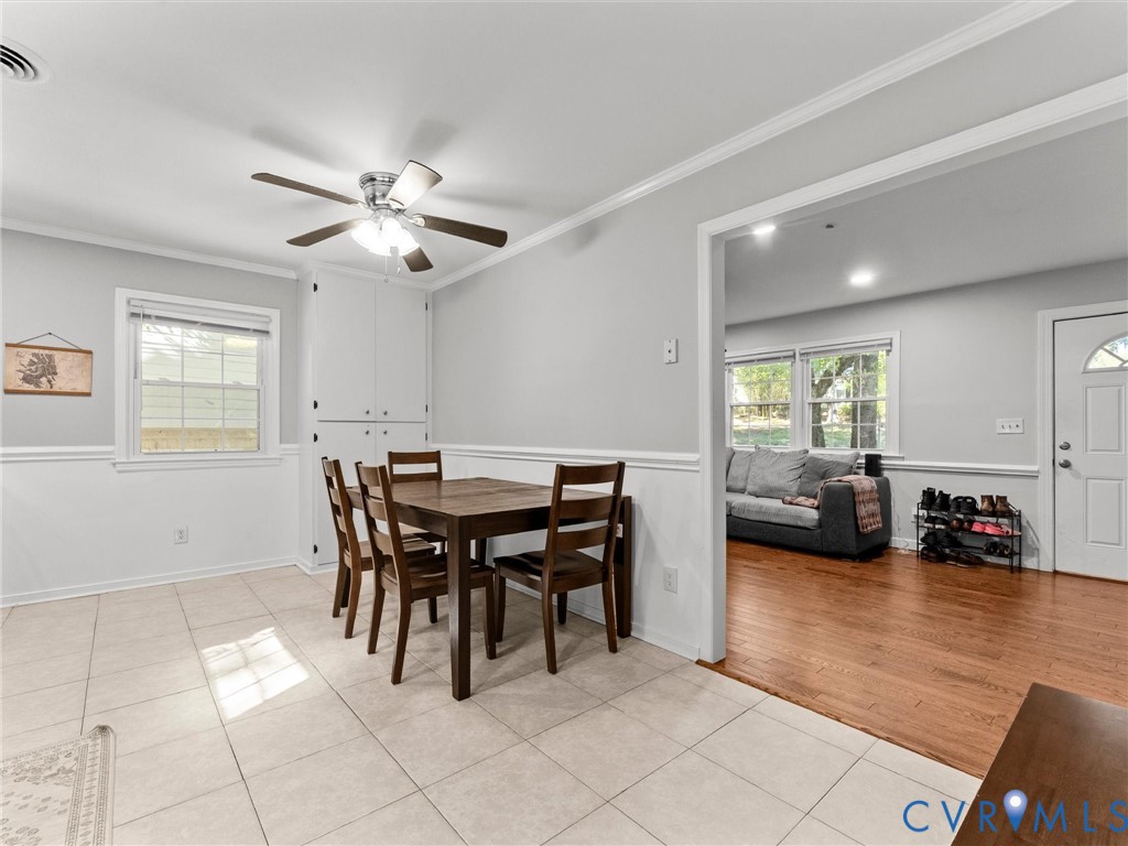 Dining area featuring large-format neutral tile flooring, built-in floor-to-ceiling cabinetry, chair rail molding, and a multi-blade ceiling fan with integrated lighting