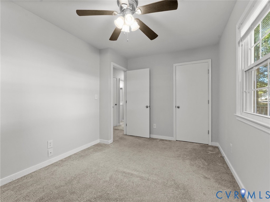 Neutral-toned wall paint, neutral carpeting, multi-light ceiling fan, and a multi-pane window
