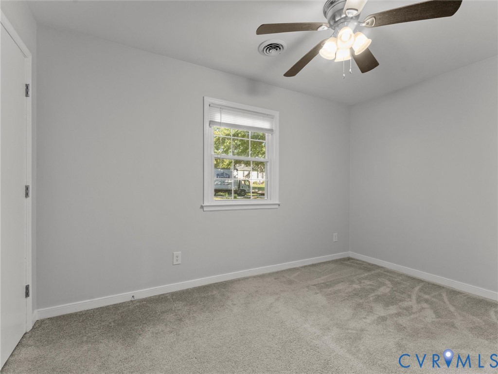 Neutral-toned interior featuring wall-to-wall carpeting, a multi-pane window with blinds, and a ceiling fan with integrated lighting