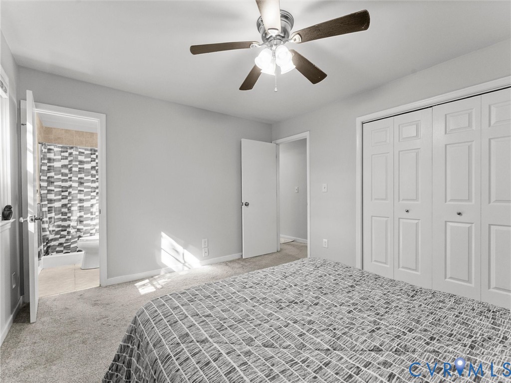 Neutral-toned carpet flooring, ceiling-mounted light fixture with multi-blade fan, and white-paneled bi-fold closet doors