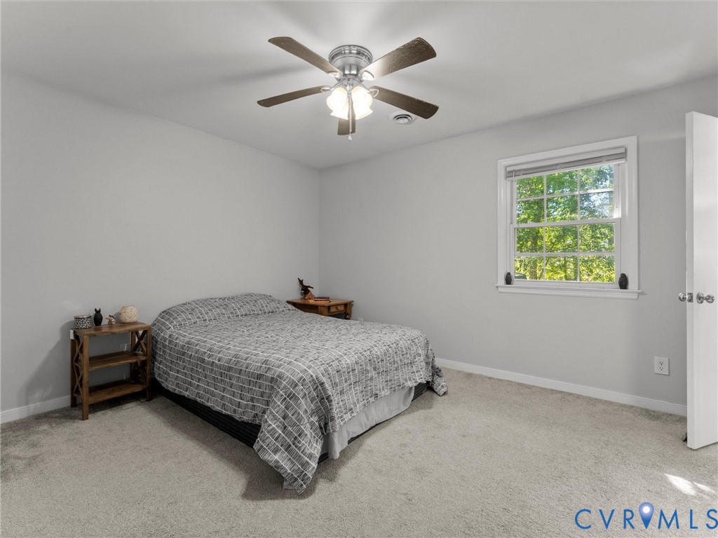 Neutral-toned interior space featuring wall-to-wall carpeting, a multi-blade ceiling fan with integrated lighting, and a double-hung window