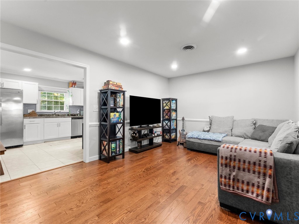 Interior space featuring wood-finish flooring, recessed lighting, and chair rail molding, with a kitchen area showcasing white cabinetry and stainless steel appliances