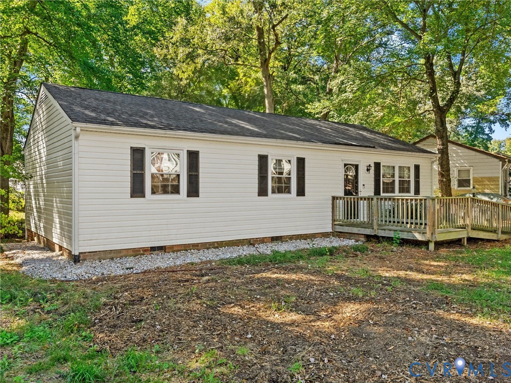 Exterior featuring white vinyl siding, dark shutters, an asphalt shingle roof, and a wooden deck with a built-in ramp