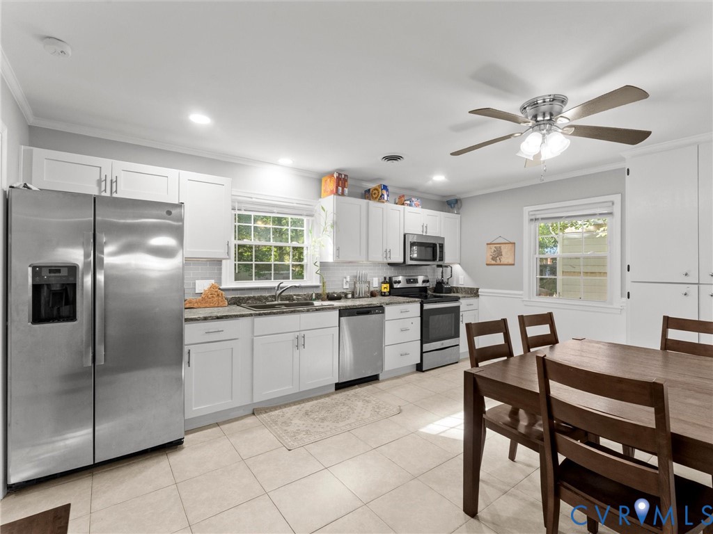Kitchen featuring white shaker-style cabinetry, stainless steel appliances, tiled flooring, solid-surface countertops, and a ceiling fan with integrated lighting