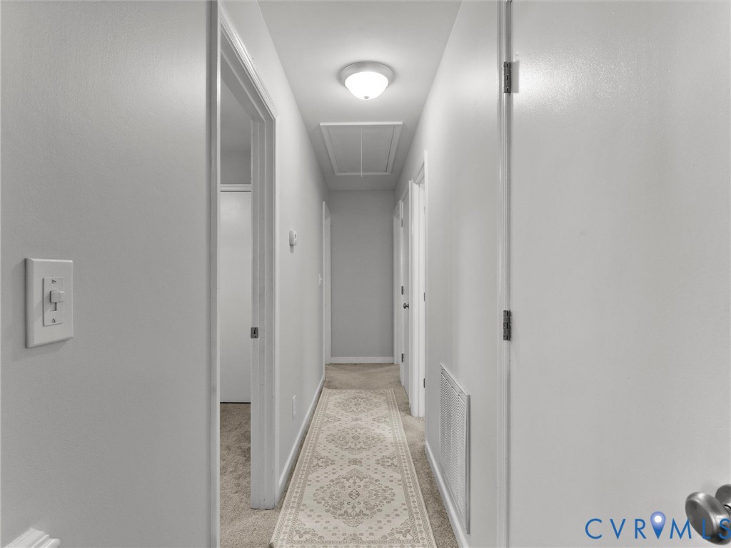Hallway featuring neutral-toned carpeting, white interior doors, and a flush-mount ceiling light fixture