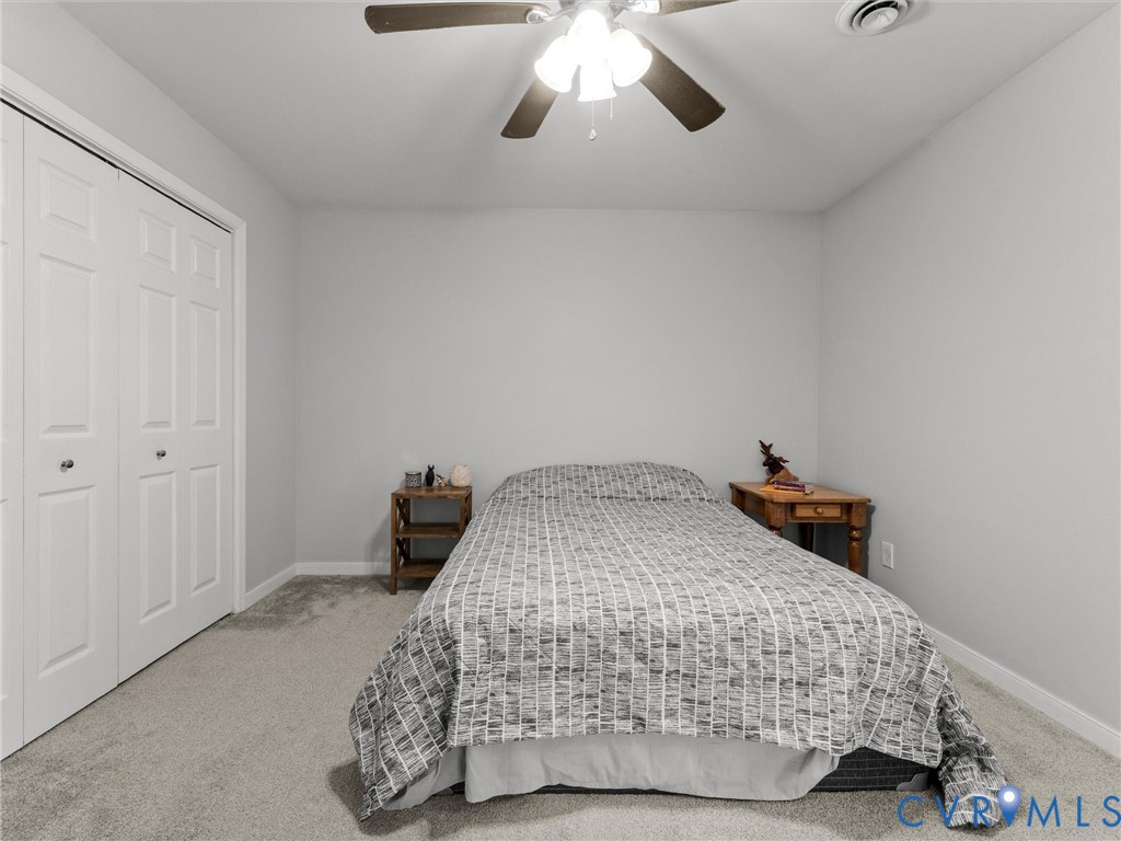Neutral-toned room featuring neutral wall-to-wall carpeting, white dual-panel closet doors, and a ceiling-mounted light fixture with a multi-blade fan