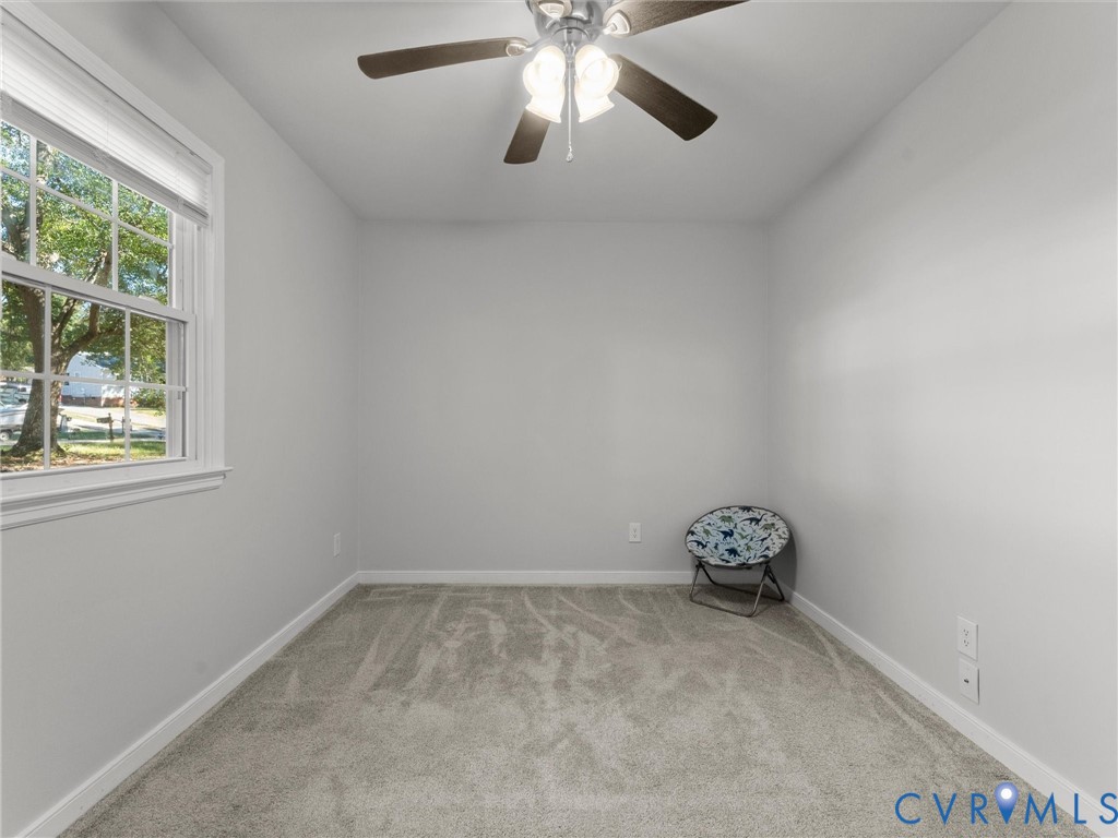 Neutral wall tones, wall-to-wall carpeting, double-hung window, and a ceiling fan with integrated light fixture