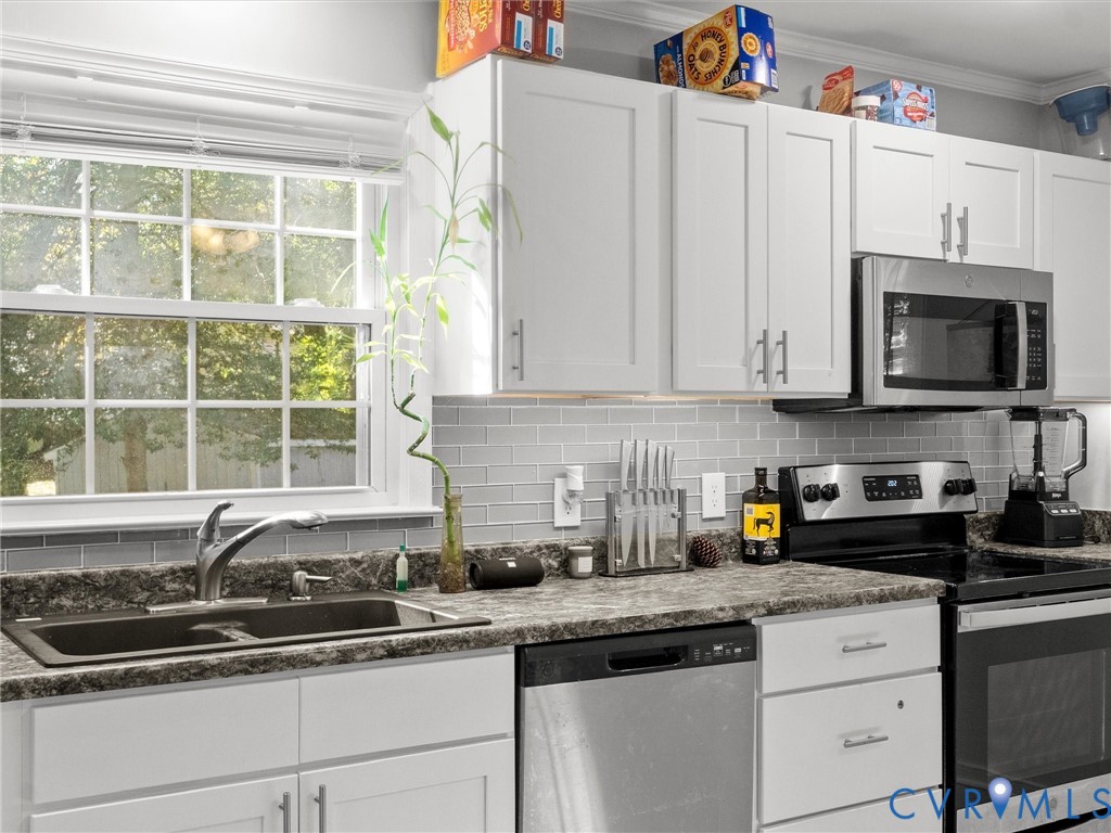 Kitchen featuring white shaker-style cabinetry, a gray subway tile backsplash, stone-finish countertops, stainless steel appliances, and a double-basin sink