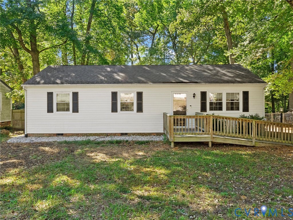 Single-story exterior featuring white vinyl siding, dark shutters, a gabled roofline, and a wood-deck ramp