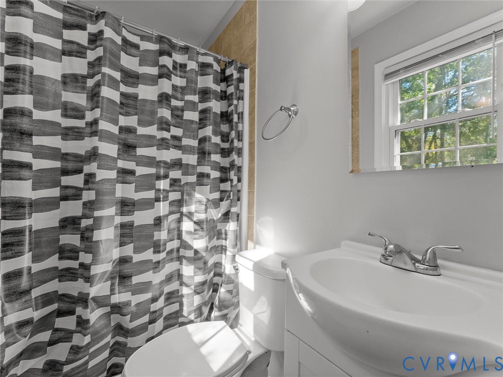 Bathroom featuring a white vanity cabinet, ceramic sink with a dual-handle faucet, wall-mounted mirror, and tile surround in the shower area