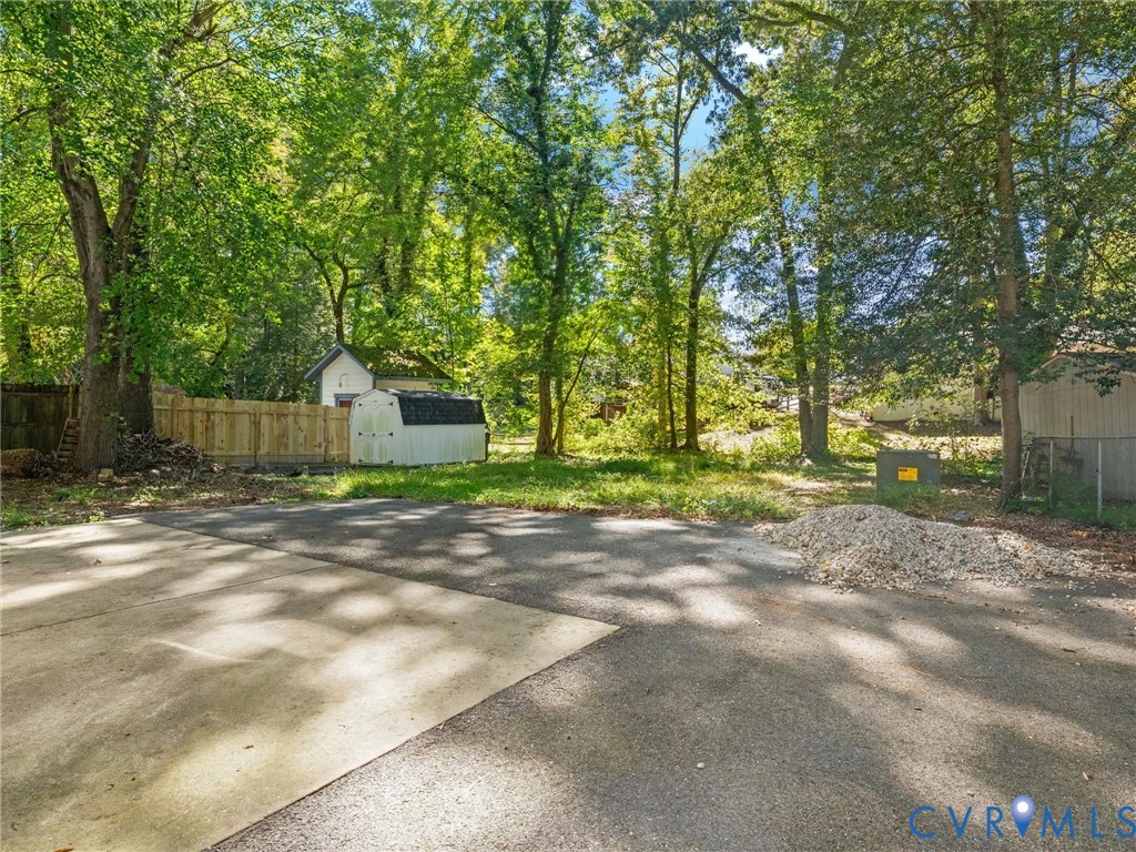 Asphalt and concrete surface, wood privacy fencing, and mature trees on a lot featuring a detached storage structure