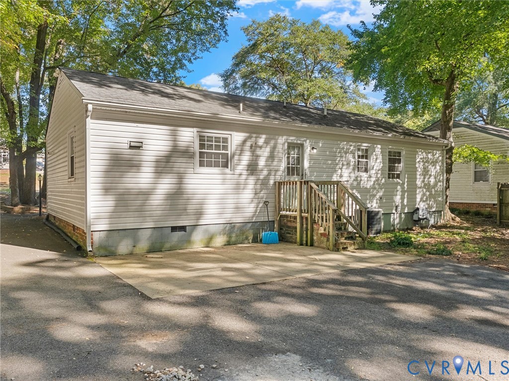 Light-colored vinyl siding exterior, concrete patio surface, timber-constructed staircase, and asphalt paved driveway