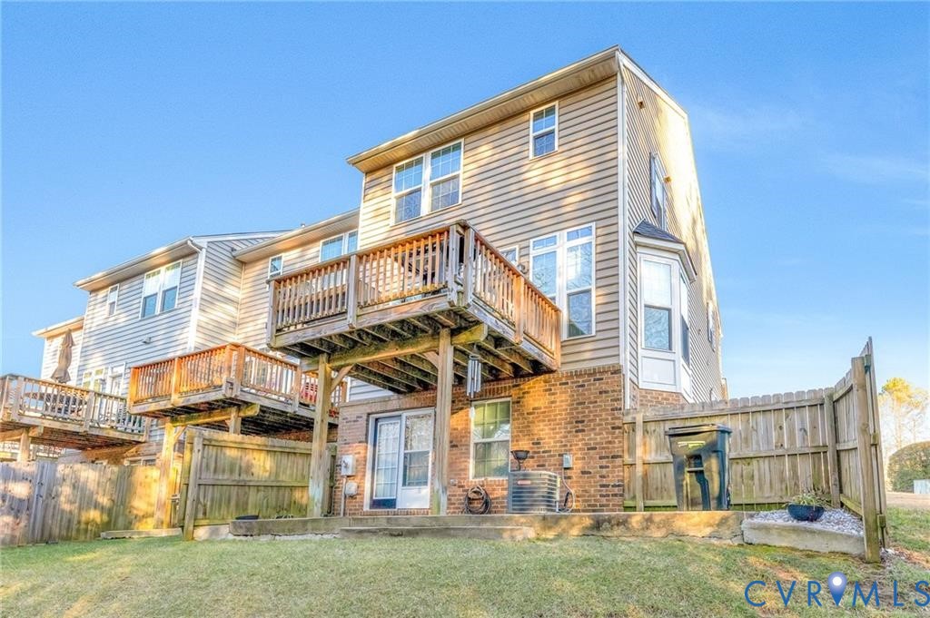 Rear view of property featuring a deck, a yard, fence, and brick siding
