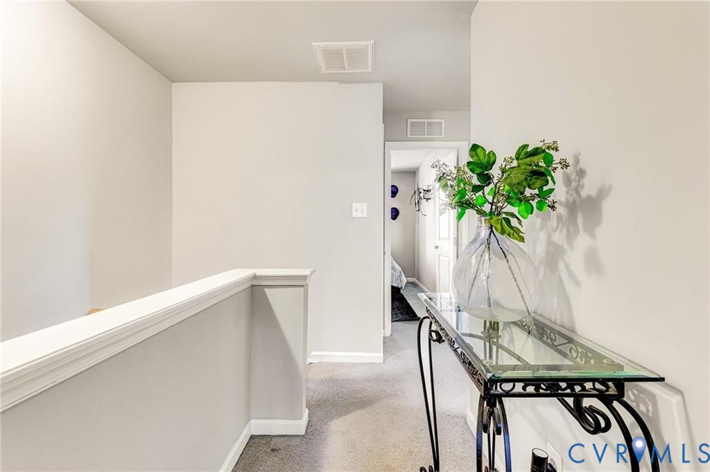 Hallway with an upstairs landing, carpet, visible vents, and baseboards