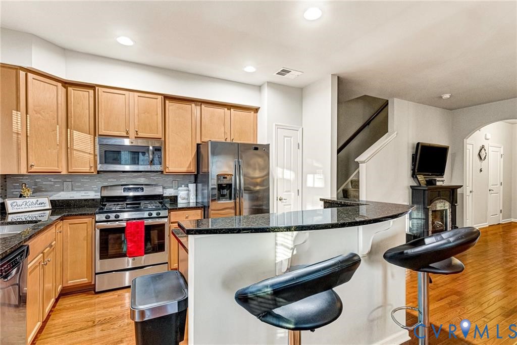 Kitchen with tasteful backsplash, a breakfast bar area, appliances with stainless steel finishes, light wood-style floors, and arched walkways Kitchen with tasteful backsplash, a breakfast bar area, appliances with stainless steel finishes, light wood-style floors, and arched walkways