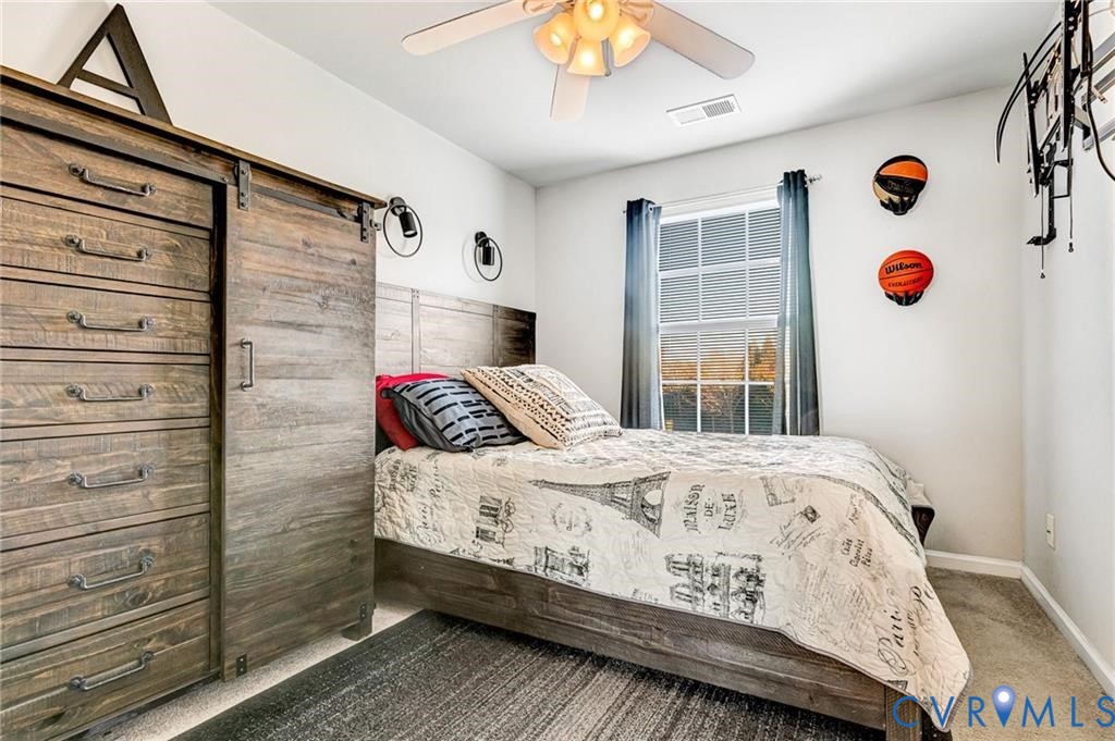 Carpeted bedroom featuring visible vents, baseboards, a barn door, and a ceiling fan