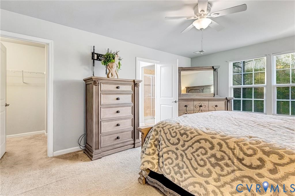 Bedroom featuring a spacious closet, baseboards, light colored carpet, a closet, and a ceiling fan