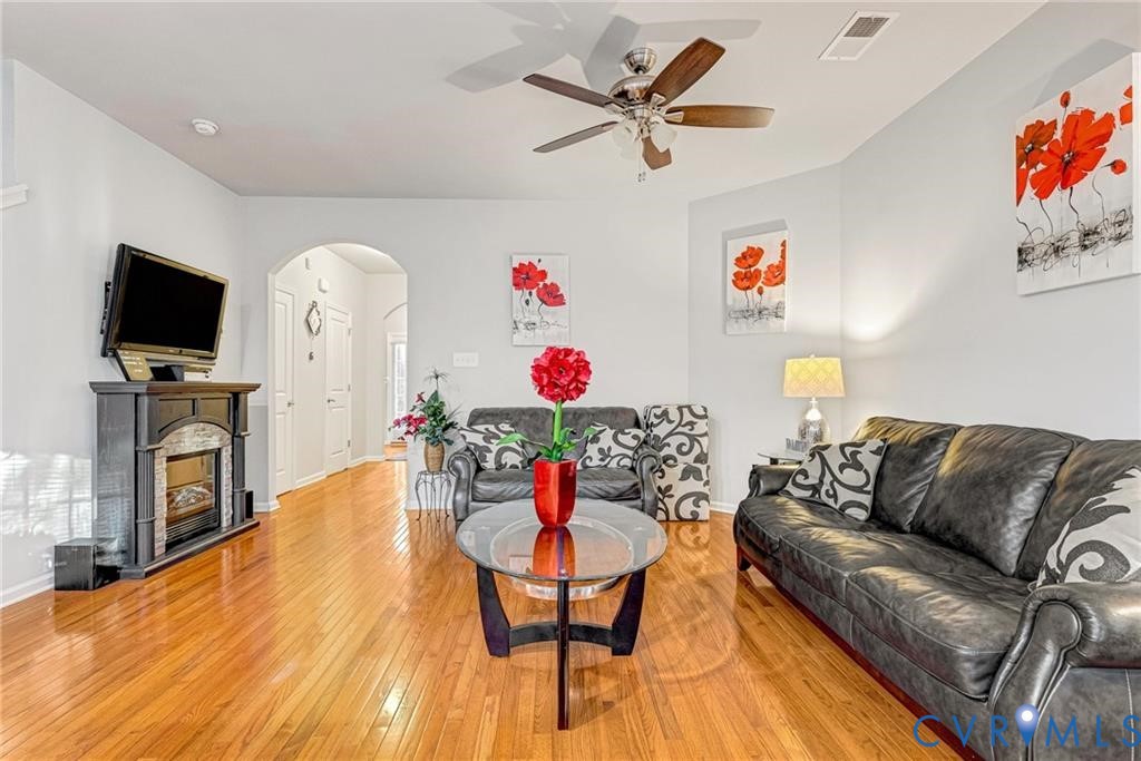 Living area featuring light wood-type flooring, visible vents, a ceiling fan, arched walkways, and baseboards Living area featuring light wood-type flooring, visible vents, a ceiling fan, arched walkways, and baseboards
