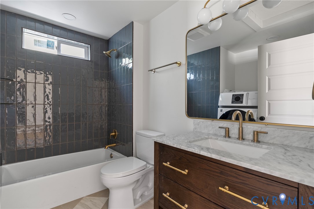 Bathroom featuring a dark wood-finish vanity with a stone countertop, an integrated rectangular sink, gold-tone hardware, a large framed wall mirror, and a tub-shower combination accented by dark vertical wall tiling