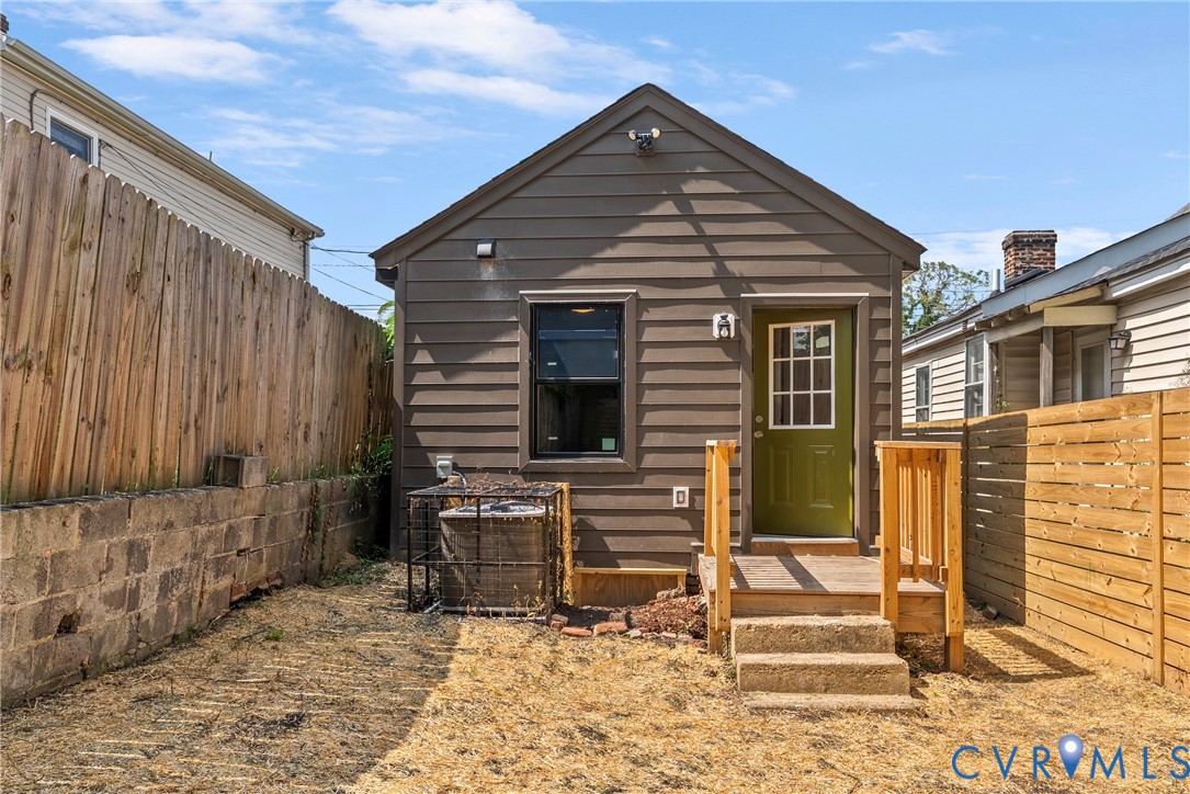 Exterior elevation featuring horizontal siding, a rear wood deck with concrete steps, and a fenced backyard with a stone retaining wall