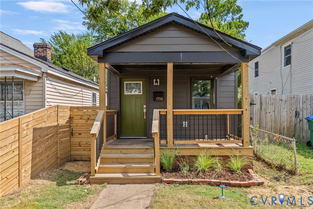 Dark-toned lap siding exterior featuring a covered front porch with natural wood posts, iron railing, and a vibrant green front door