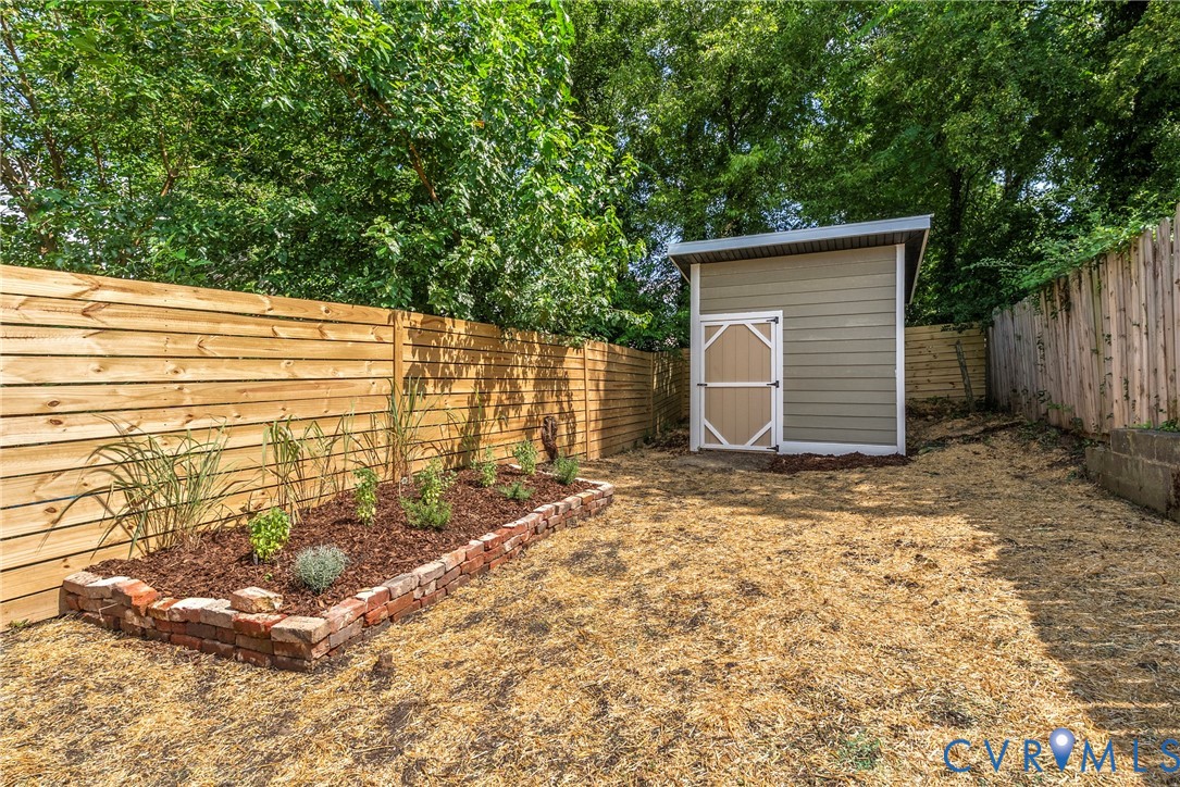 Rear yard featuring a detached storage shed, horizontal wood privacy fencing, and a raised brick-bordered garden bed