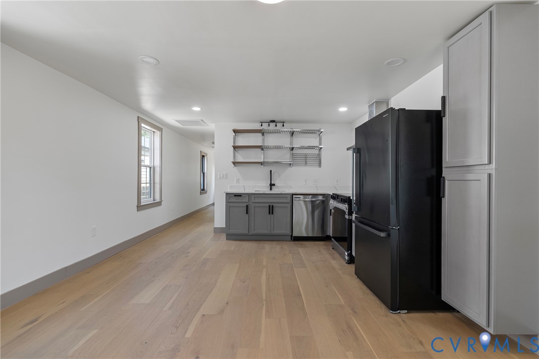 Kitchen featuring wood-finish flooring, charcoal shaker-style cabinetry, matte black hardware, stainless steel appliances, and open wall-mounted shelving