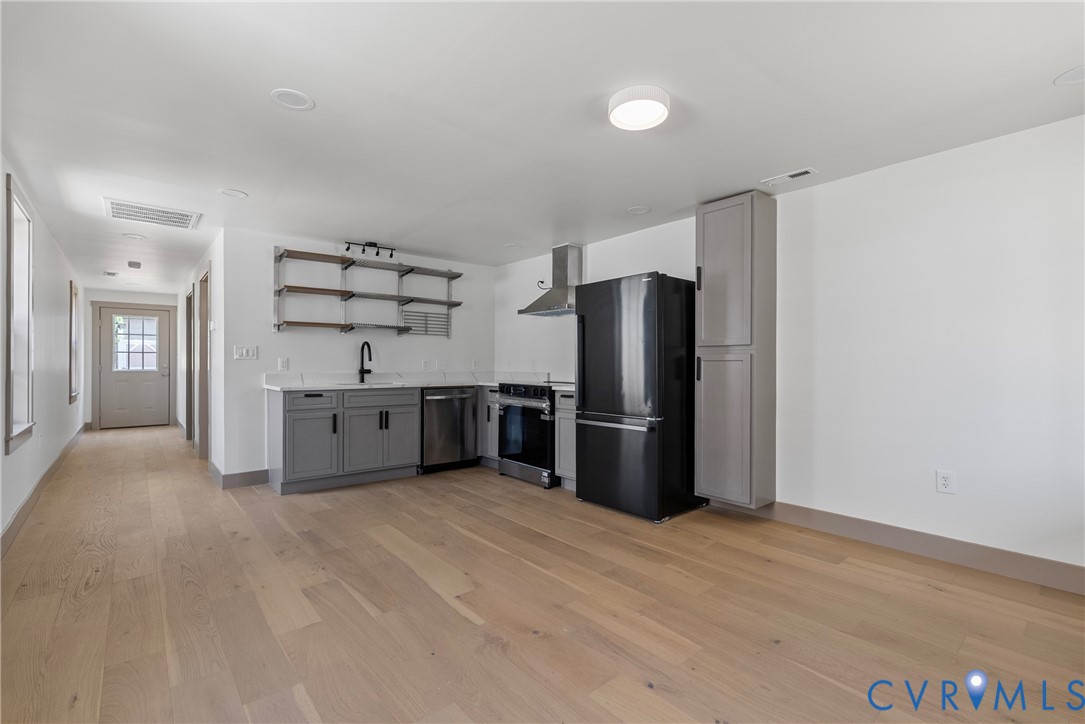 Kitchen featuring wood-finish flooring, grey cabinetry, solid-surface countertops, open metal shelving, and stainless steel appliances