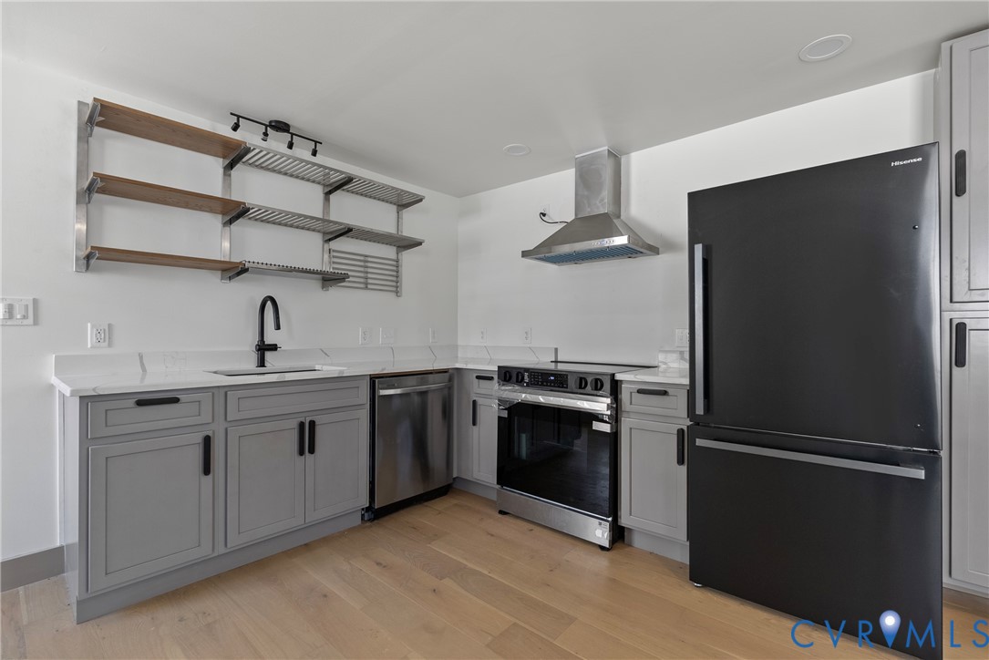 Kitchen featuring light gray shaker-style cabinetry, white countertops with matching backsplash, stainless steel appliances, wood-finish flooring, and open metal shelving