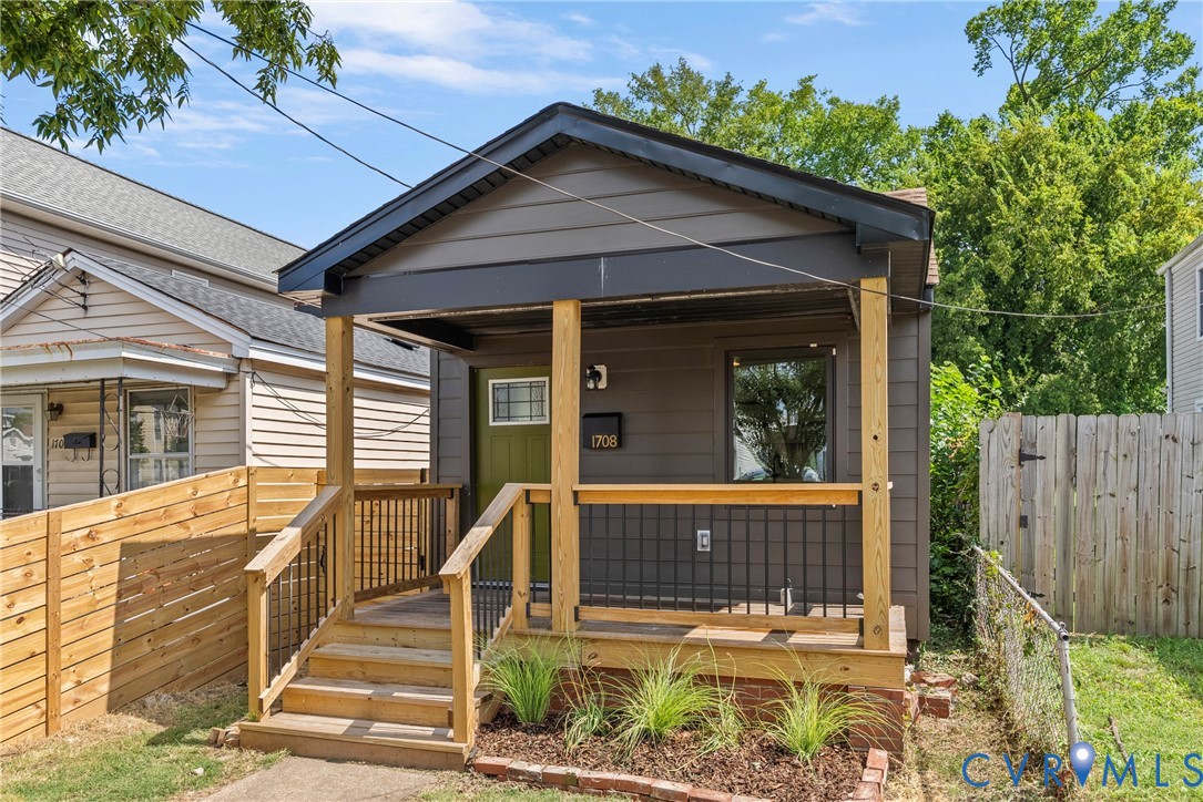 Exterior featuring horizontal siding, a covered front porch with natural wood posts and railings, black metal balusters, and a solid-color entry door with an upper glass pane