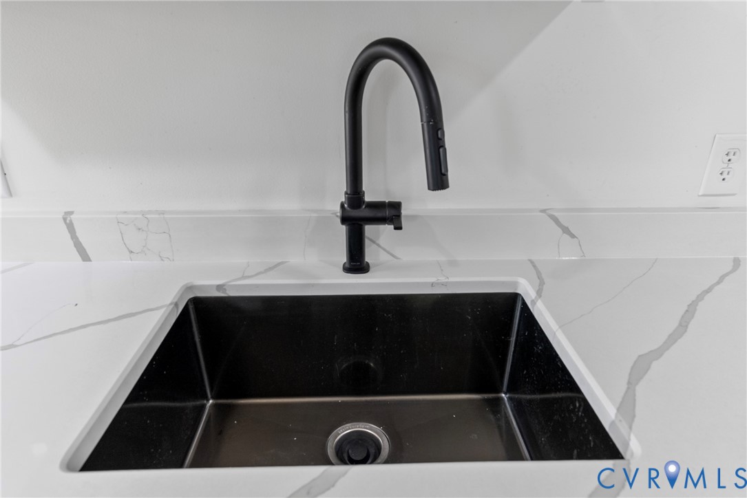Undermount deep-basin sink with a matte black high-arc pull-down faucet, set into a stone-finish countertop with an integrated backsplash
