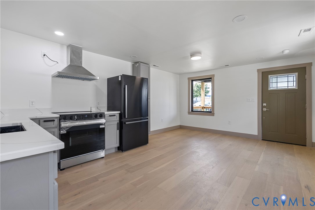 Kitchen featuring wood-finish flooring, light-toned cabinetry, quartz countertops, stainless steel range hood, and black kitchen appliances