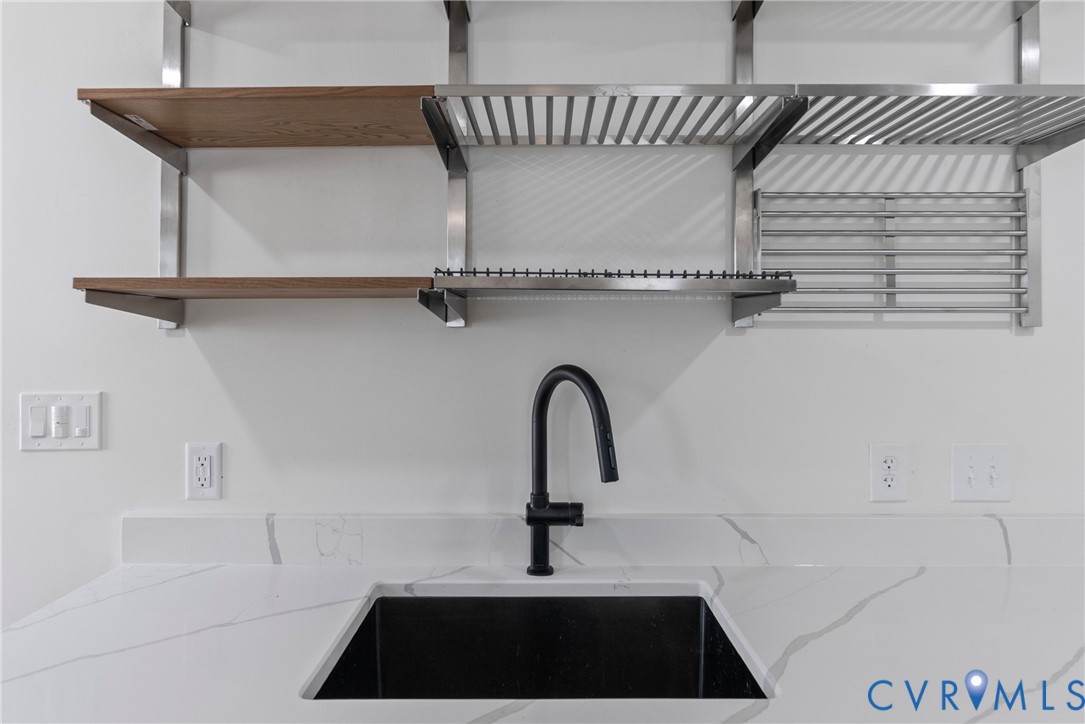 Undermount sink with a matte black gooseneck faucet, white stone-patterned countertop with matching backsplash, and industrial-style shelving featuring metal racking and wood-finish accents