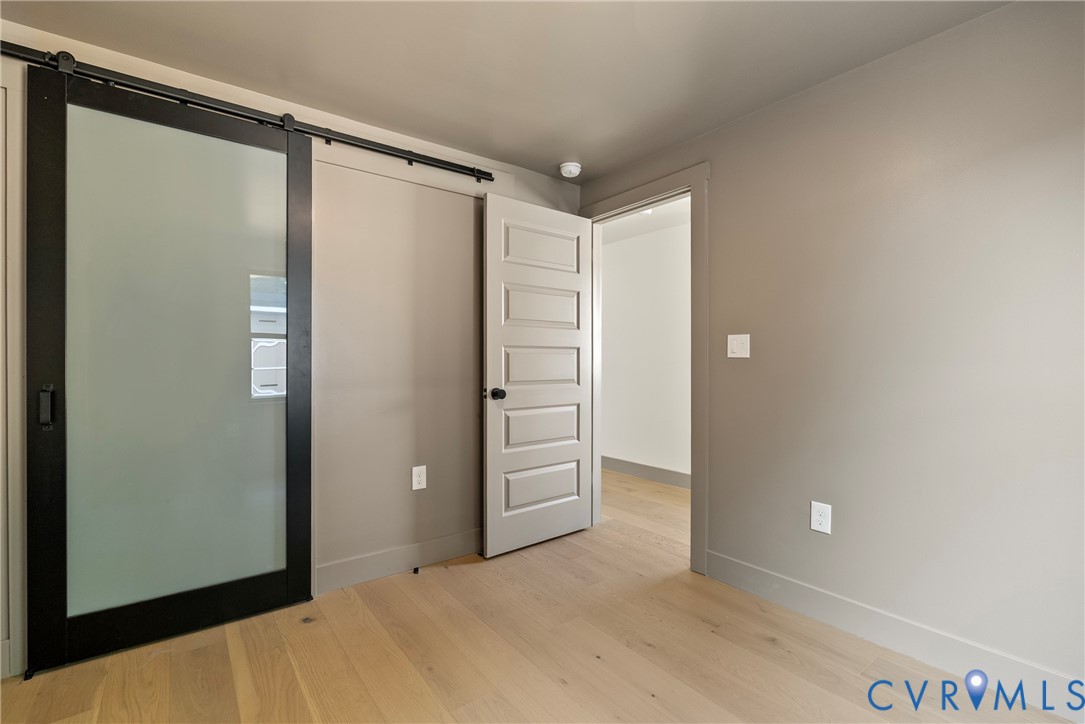Sliding door with a black frame and frosted glass panel, five-panel interior door with matte black hardware, and wood-finish flooring