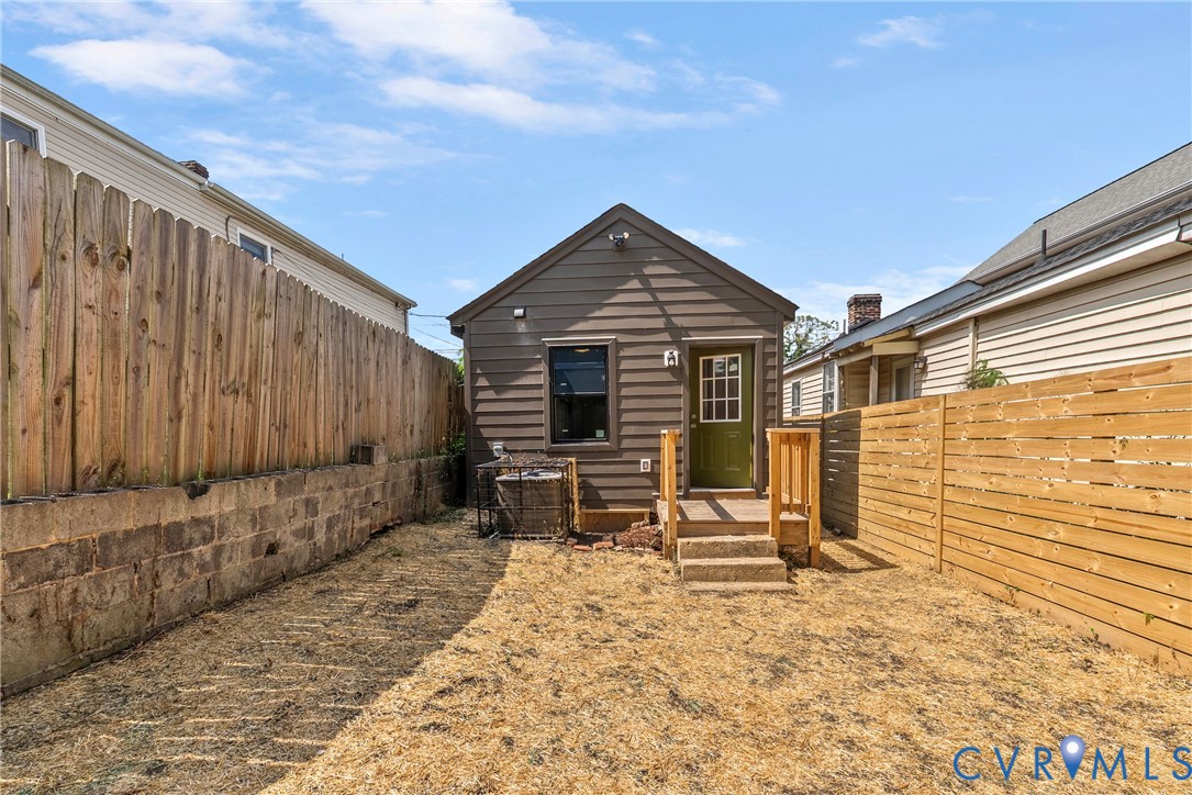 Rear exterior featuring horizontal siding, a wooden staircase, a solid-paneled door with glass upper light, a stone retaining wall, and wood privacy fencing