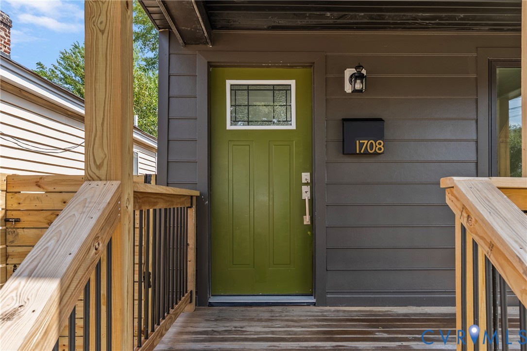 Covered front porch featuring wood-finish decking, dark horizontal siding, a solid entry door with a rectangular window pane, and modern metal railings